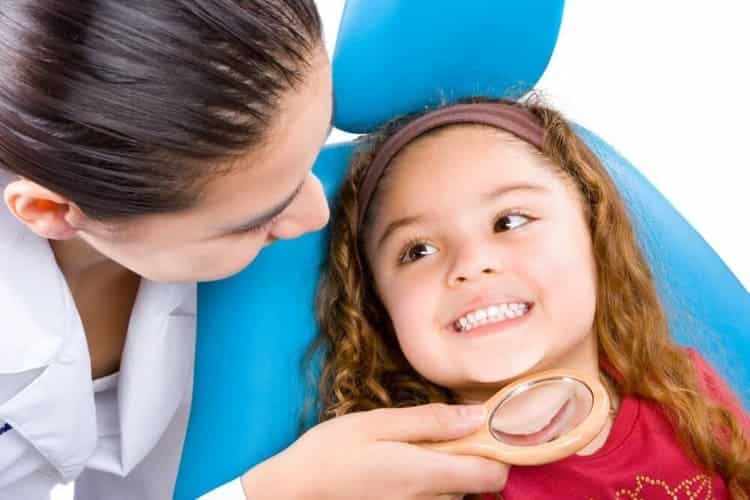 odontopediatria doctora mirando a niña pequeña en un sillon azul